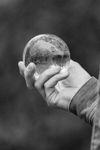 istock Vertical grayscale shot of a person's hand holding a crystal-clear sphere 1435348244
