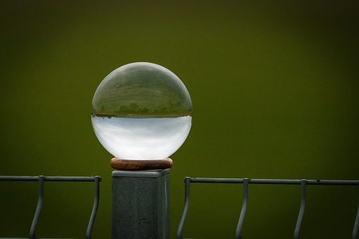 A closeup of a perfect sphere crystal on a metal post and reflecting the surroundings inversely