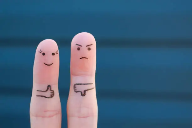 Photo of Fingers art of couple. Woman showing thumbs up and man showing thumbs down. Concept of disagreement in family.