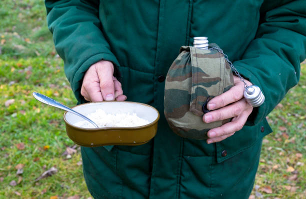 mężczyzna trzyma w rękach wojskową butelkę wody i melonik wojskowy z owsianką i łyżką do zbliżenia - military canteen zdjęcia i obrazy z banku zdjęć