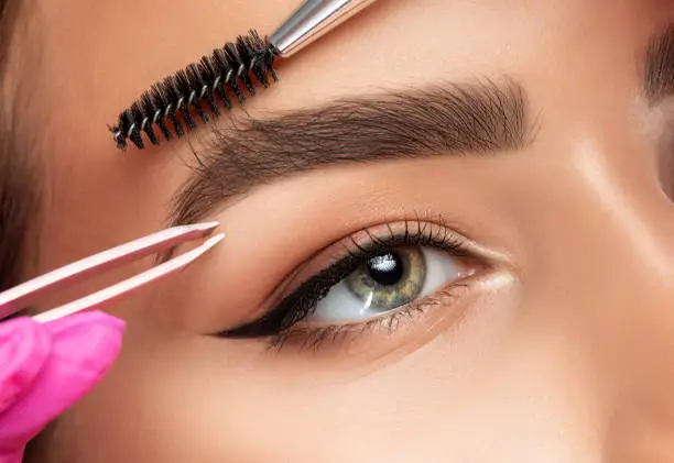 Photo of Makeup artist plucks eyebrows. Long-lasting styling of the eyebrows and color the eyebrows. Eyebrow lamination. Professional make-up and face care.