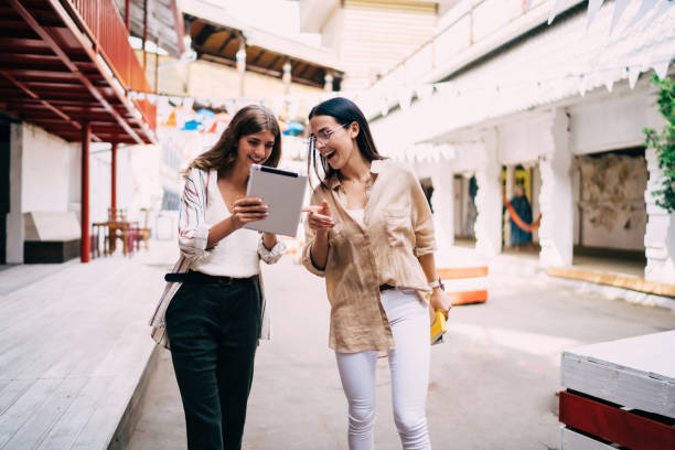 istock Cheerful female friends enjoying urban walking and networking time using 4g wireless on modern touch pad, sincerely hipster girls browsing website with funny publication laughing from content 1435351206