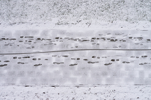 Maintenance of streets and sidewalks in winter. Light snowy sidewalk and human footprints on pedestrian path. Aerial view.
