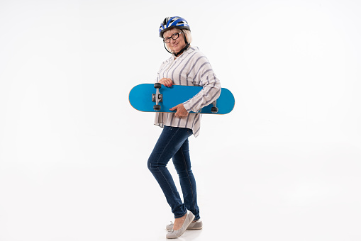 Bearded guy holding a longboard and leaning against a gray wall