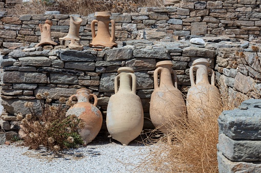 A set of amphoras near the rocky brick wall outdoors of Delos Island,  Greece