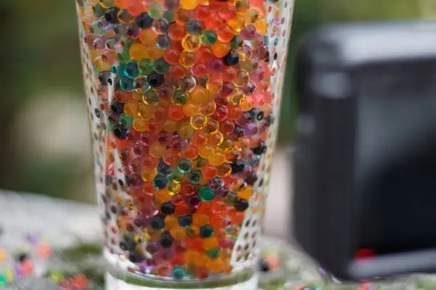 Close up on a glass filled with colored balls. An action camera set vertically on a tripod is recording the scene.