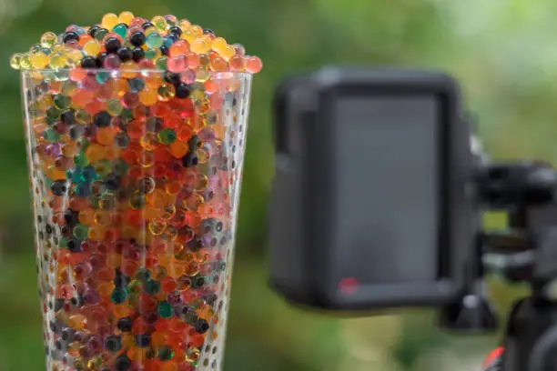 Close up on a glass filled with colored balls. An action camera set vertically on a tripod is recording the scene.