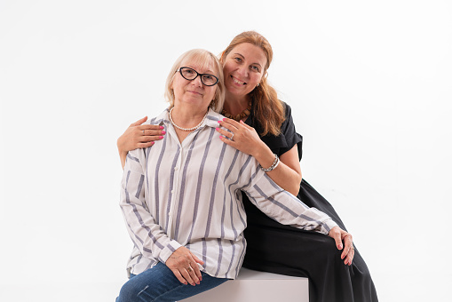 Portrait of smiling daughter and mother embracing against white background.