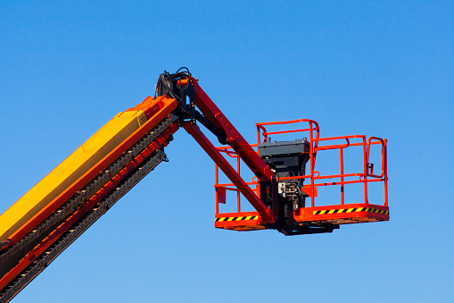 Colorful yellow and red cherry picker, clear blue sky background. Low angle view. Galicia, Spain.