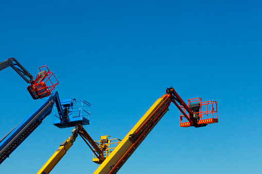 Three colorful cherry pickers, clear blue sky background. Low angle view. Galicia, Spain.