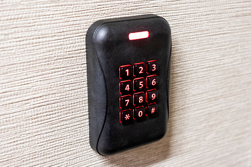 A side view angle close up photograph of a black security system keypad with numbers illuminated in red.