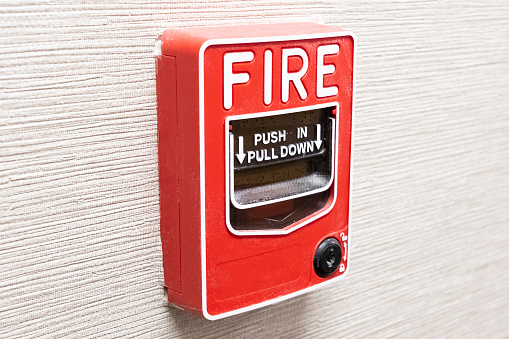 A side angle view of a bright red fire alarm mounted on an office wall.