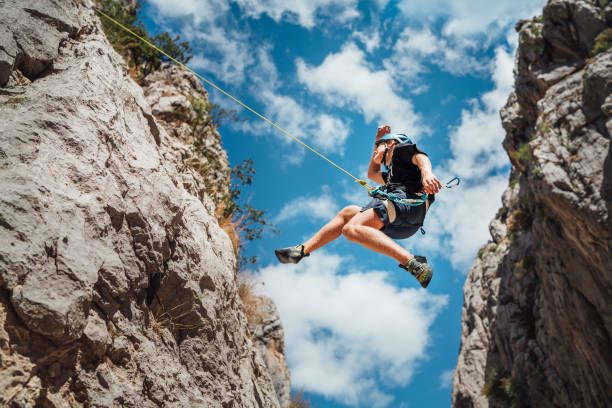 Climber teenage boy in protective helmet jumping on vertical cliff rock wall using rope Belay device, climbing harness in Paklenica canyon in Croatia. Active extreme sports time spending concept