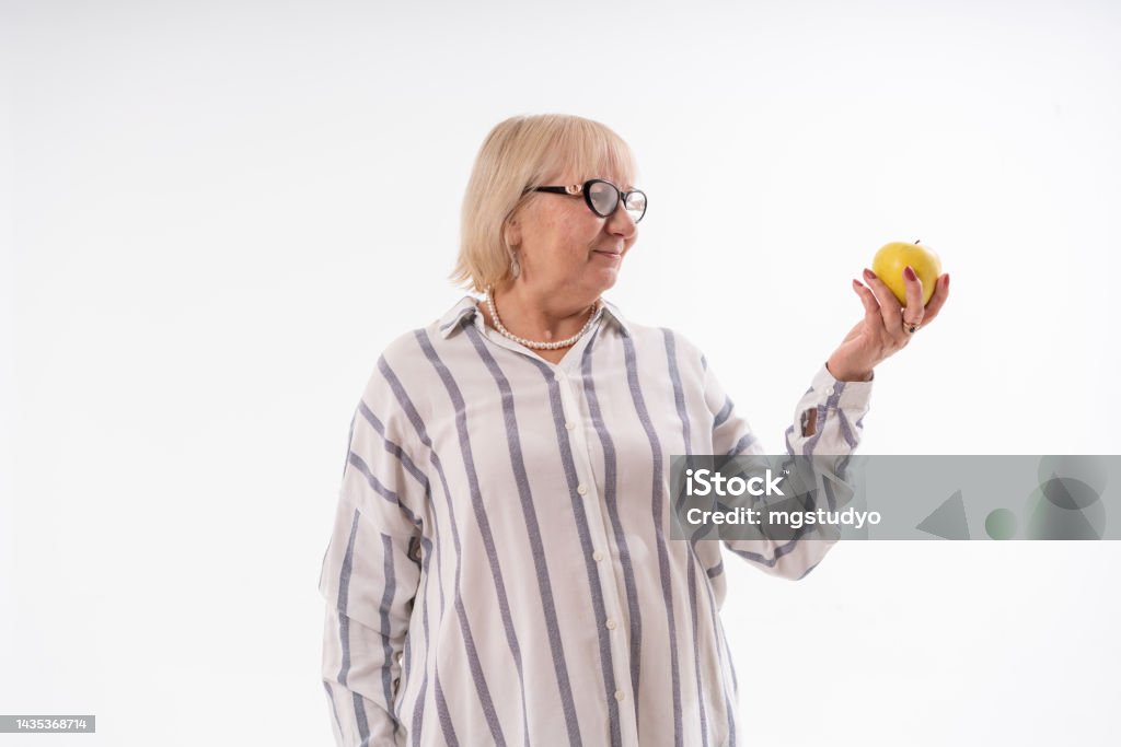 Senior woman holding an apple against white background. 70-79 Years Stock Photo
