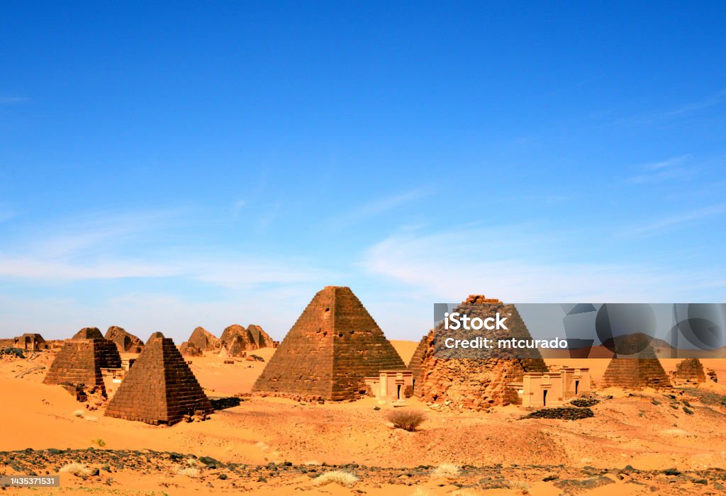 Meroe pyramids and Sahara desert, South and North cemeteries (foreground and background) Meroë, Begarawiyah, Kush, Sudan: Nubian pyramids of Meroe, tombs of the Kushite kingdoms - South Necropolis and North Necropolis (foreground and background respectively) - located 200 kilometers northeast of Khartoum near the village of Bagrawiya, spread over small hills. In total there are more than 900 pyramids and tombs. The pyramids, mostly built of stone, are significantly smaller than the Egyptian pyramids with a height of less than 30 meters and served as burial places for the kings, queens and high officials of the historical empire of Kush in Nubia. Construction ranges from around 300 BC to about AD 300. The first pyramid at Meroe that can be attributed to King Ergamenes, who died about 280 BC. Nubian Desert Stock Photo