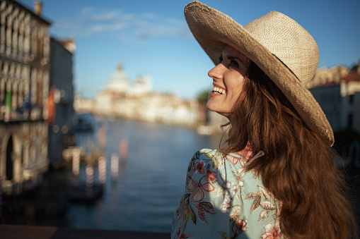 happy young traveller woman in floral dress with hat having walking tour on Accademia bridge in Venice, Italy.