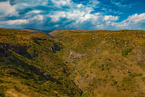 Rocky canyon near Amberd fortress with dramatic clouds, in summer. Spectacular clouds over a canyon covered with rocks and bushes.