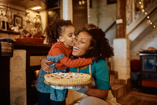 Affectionate  mother and daughter with freshly baked holiday pie in the kitchen. African American mother getting a kiss from her daughter after baking sweet pie in the kitchen. black family home stock pictures, royalty-free photos & images