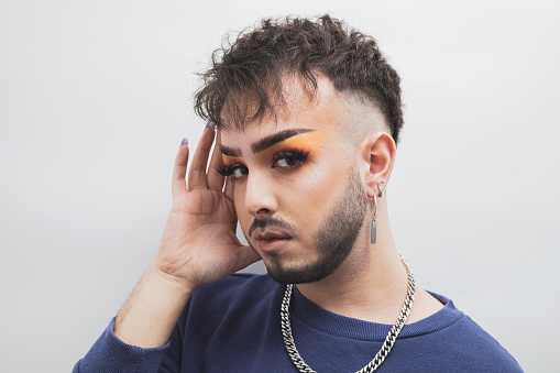 a portrait of a young man in makeup posing on a white background with one hand on his face.diversity concept.