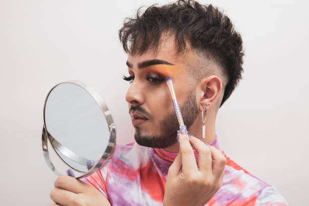 istock A young gay man putting on makeup with a mirror on a white background. 1435383575