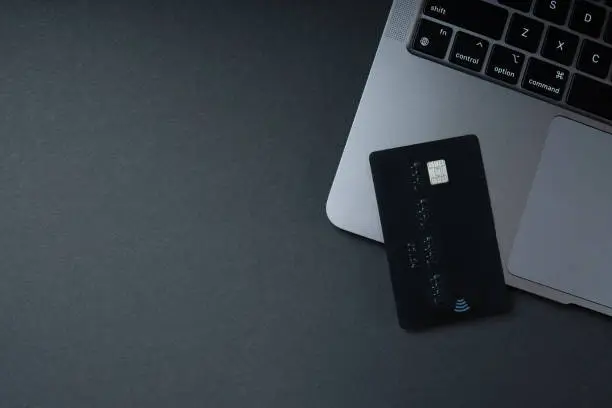 Credit card lying near the laptop on a dark bacground. Online shopping, business, e-commerce concept. Copy space.