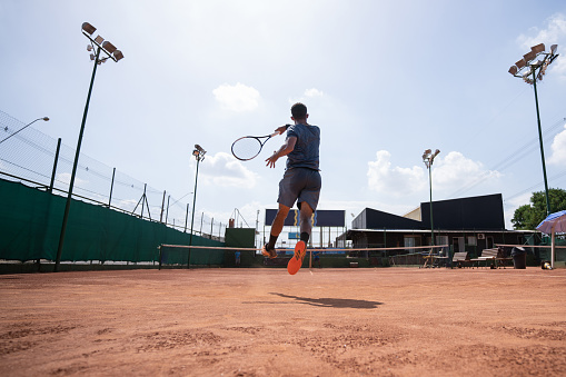 Young man playing tennis with his friend, they are having fun and vying every moment.