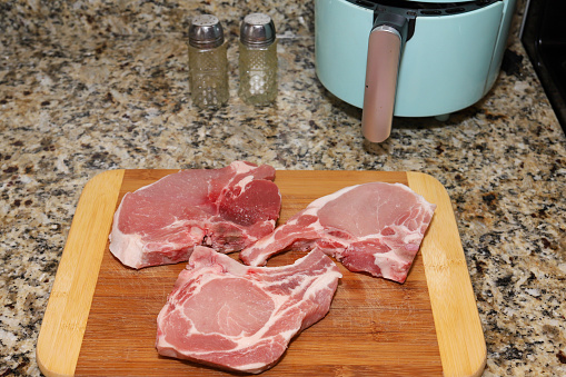 Uncooked pork chops on a wooden cutting board