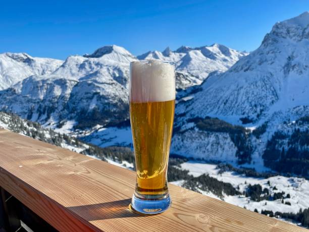 apres esquia en los alpes austríacos. vaso de cerveza de trigo en una valla de madera en un día soleado. estación de esquí de lech zuers, parte de la zona de esquí de arlberg. - apres ski ski snow mountain fotografías e imágenes de stock