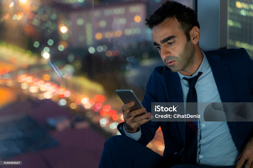 tired officer working night shift in office. officer is using the phone tired officer working night shift in office. officer is using the phone. city ​​lights and car headlights are out of focus. 
city ​​view seen from the window. Shot with a full frame camera. 35-39 Years Stock Photo