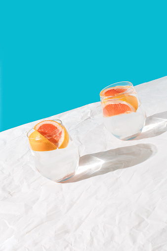 Two glasses water with pieces grapefruit on turquoise blue background. Light summer colors. Minimal creative idea.
