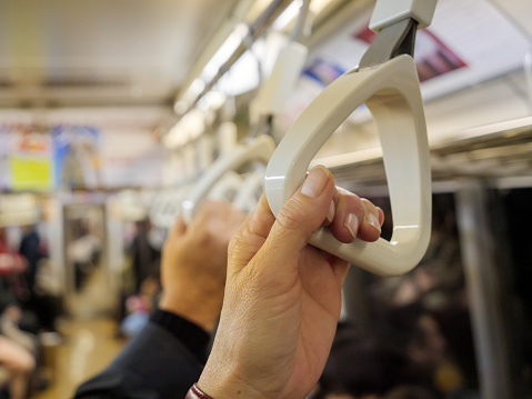 Hands holding on to handles to support themselves while standing on a busy subway train.