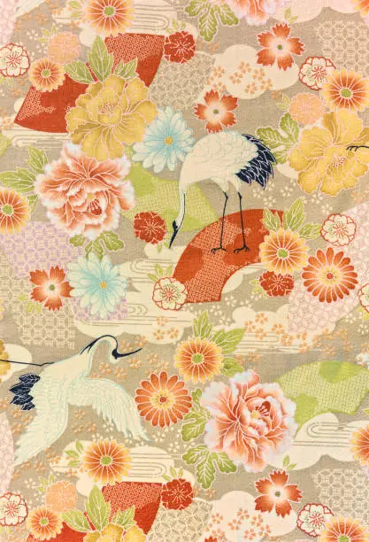 Closeup detailed photograph of a traditional Japanese furoshiki cloth depicting flying tsuru cranes symbol of luck and longevity surrounding by cherry, plum,cosmos,chrysanthemums or roses flowers.