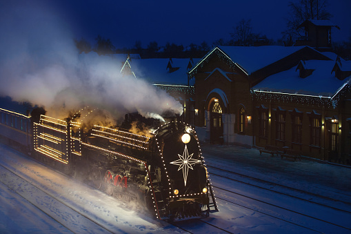 festively decorated with lights retro Christmas train on rails, snowy evening