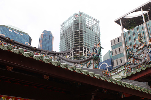 Part of the roof of the Thian Hock Keng Chinese temple in Telok Ayer Street in  Singapore's Chinatown district with tall modern buildings of Singapore's financial district in the background.