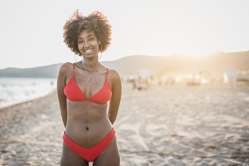 Portrait of a beautiful black woman standing on the beach in a bikini, smiling and happy