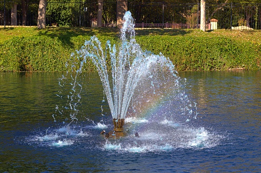 The Sun creates a partial rainbow shining through a fountain.