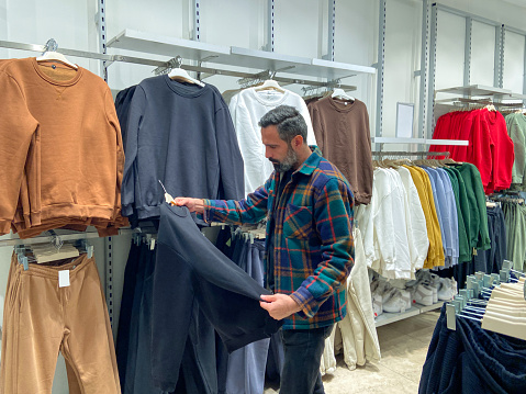 Man choosing clothes to buy in clothing store, man shopping for clothes