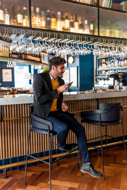 istock Young attractive man sitting at the bar while leaving a message on his smartphone 1435419176