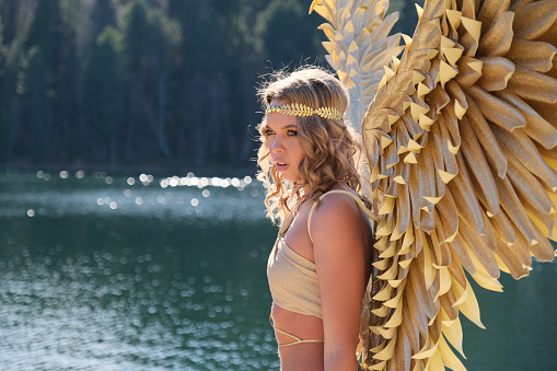 Girl dressed as an angel on the background of a forest lake