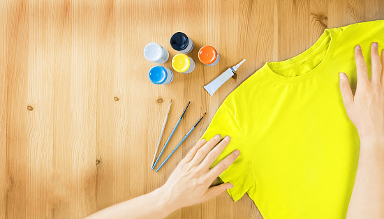 Yellow t-shirt, paints and brushes on wooden background. Selective focus