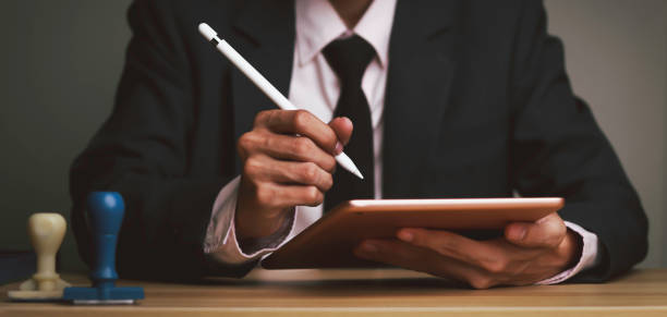 istock Businessman writes signing contract, designs, draws, or sketches projects through a tablet on the office desk. Concept stamp of approval on a public notarization certificate document electronic. 1435435633