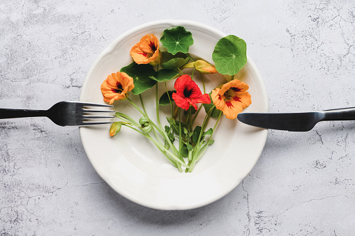 Nasturtium plants, Indian cress flowers and leaves in plate on kitchen table, top view