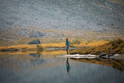 A Caucasian woman enjoys a hike on a beautiful Autumn day in Mount Baker area, Washington state, USA.  The fall colors of the Pacific Northwest are visible with vibrant red and yellow leaves on the ground cover.   Healthy and enjoyable lifestyle.