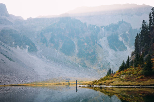 A Caucasian woman enjoys a hike on a beautiful Autumn day in Mount Baker area, Washington state, USA.  The fall colors of the Pacific Northwest are visible with vibrant red and yellow leaves on the ground cover.   Healthy and enjoyable lifestyle.