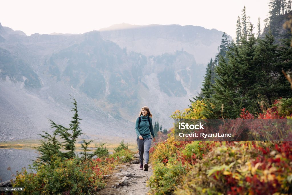 Woman Hiking In Washington State Wilderness Area A Caucasian woman enjoys a hike on a beautiful Autumn day in Mount Baker area, Washington state, USA.  The fall colors of the Pacific Northwest are visible with vibrant red and yellow leaves on the ground cover.   Healthy and enjoyable lifestyle. Pacific Northwest Stock Photo