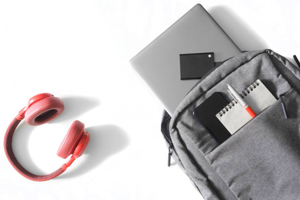 istock Gray urban backpack or bag with laptop, mobile phone, external ssd disk, notepad and pen lies on a white table next to red headphones and mouse. Tools and gadgets of a student or freelancer. 1435449305