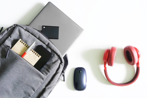 istock Gray urban backpack or bag with laptop, external ssd drive, mobile phone, notepad and pen on a white table next to mouse and red headphones. Tools and gadgets of a student or freelancer. 1435449325