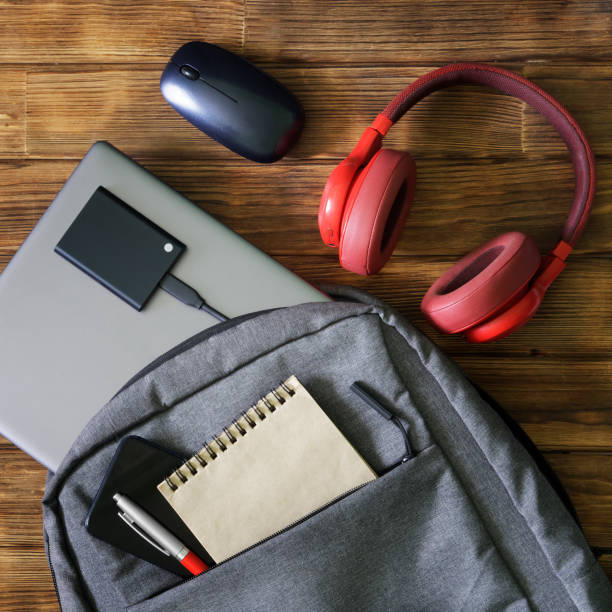 istock Gray textile backpack or bag with laptop, mobile phone, fountain pen, notepad and external ssd drive on wooden table next to red headphones and mouse. Tools and gadgets for work and study. 1435449370