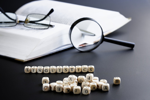 Word linguistics made up of cubes next to open book, pen, magnifying glass and glasses. Concept of studying the humanities and linguistics in school, college and university. Selective focus. Close-up