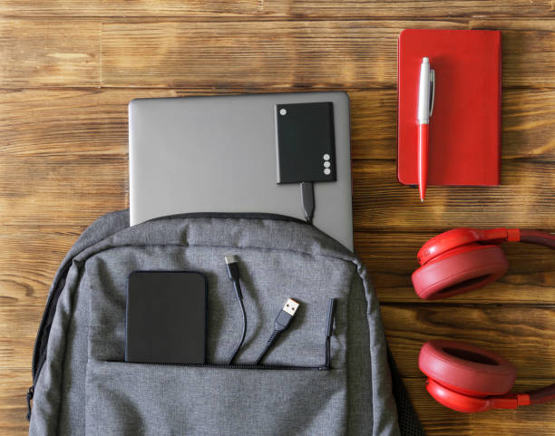 istock Gray textile urban backpack or bag with laptop, mobile phone and external ssd drive next to pen, notepad and headphones. Vintage wooden table. Accessories and gadgets for work and study. 1435449409